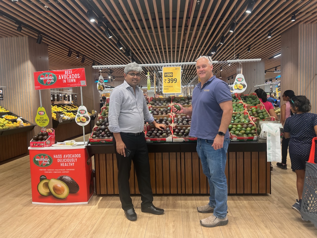 2 men standing against a display of avocados in an Indian supermarket