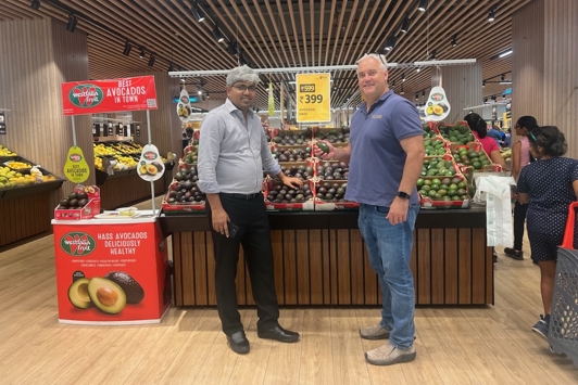 2 people standing against a display of avocados in an Indian supermarket