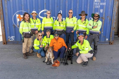 Group of people smiling wearing safety hi-vis clothing in front of sea container