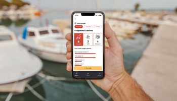 Hand holding mobile device with fishcatchwa app on screen boat yard in background
