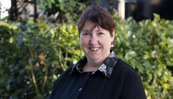 A woman smiling at the camera standing in front of foilage.